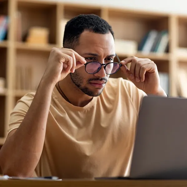 Brand stock photo of a man rubbing his eyes in front of a laptop