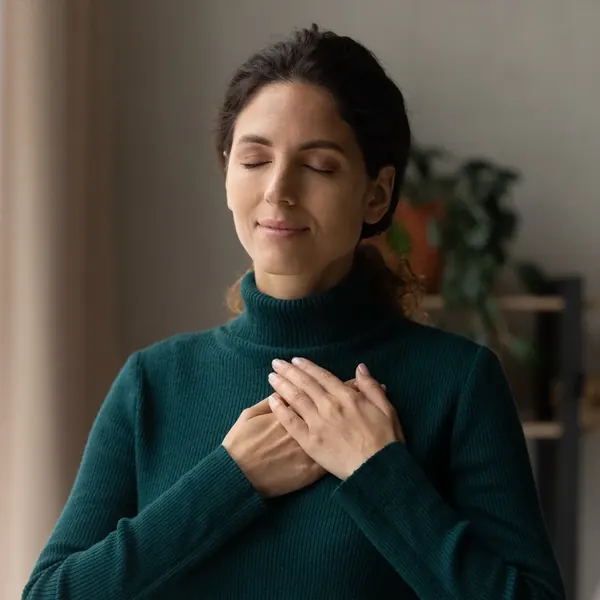 A woman with her eyes closed and both hands resting on her chest, looking calm